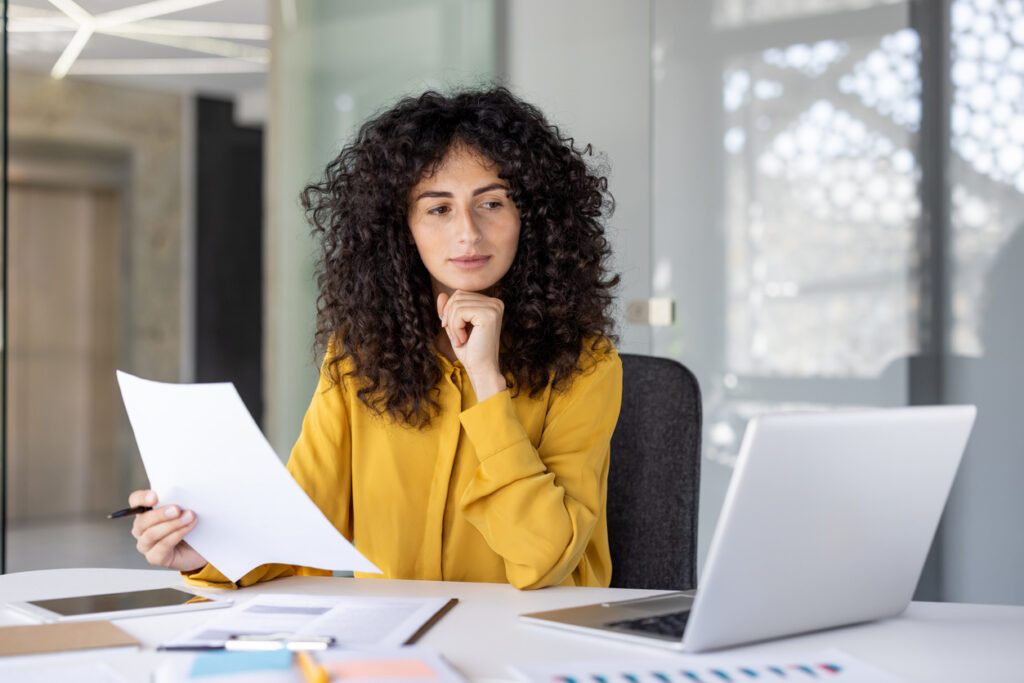 A thoughtful accountant reviews paperwork in a modern office setting, looking for discrepancies and ensuring compliance.